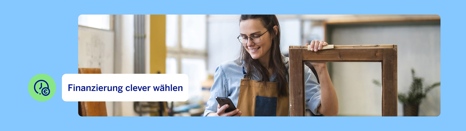 Person arbeitet in einer Werkstatt und hält einen Holzrahmen, während sie auf ein Smartphone schaut – Symbol für flexible Finanzierungsmöglichkeiten wie den Sofortkredit.