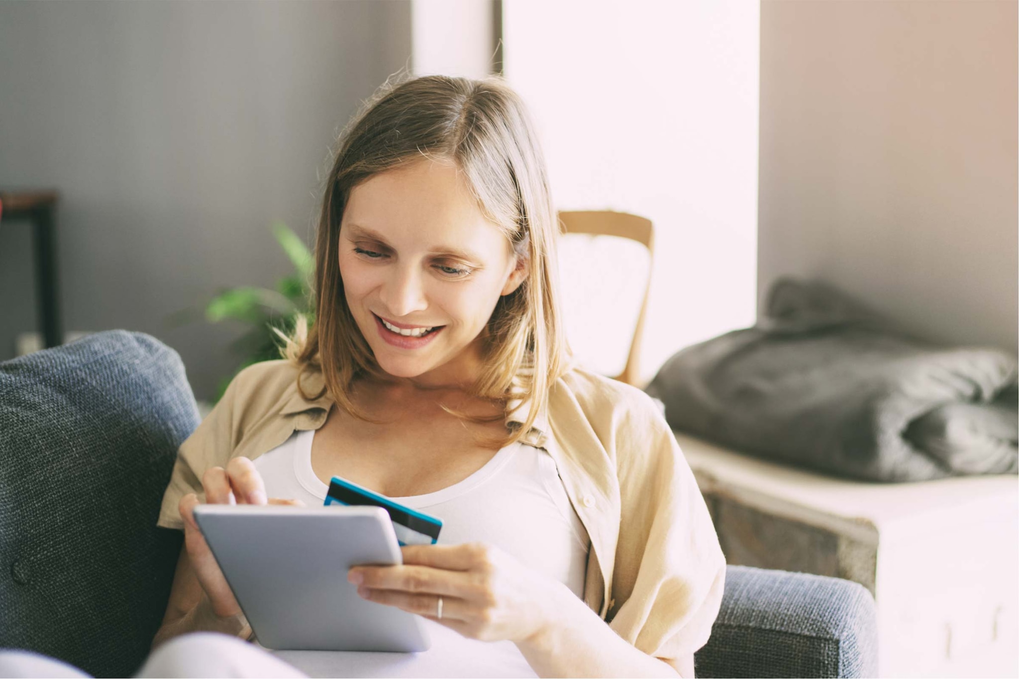 Person sitzt auf einem Sofa und nutzt ein Tablet sowie ein Smartphone.