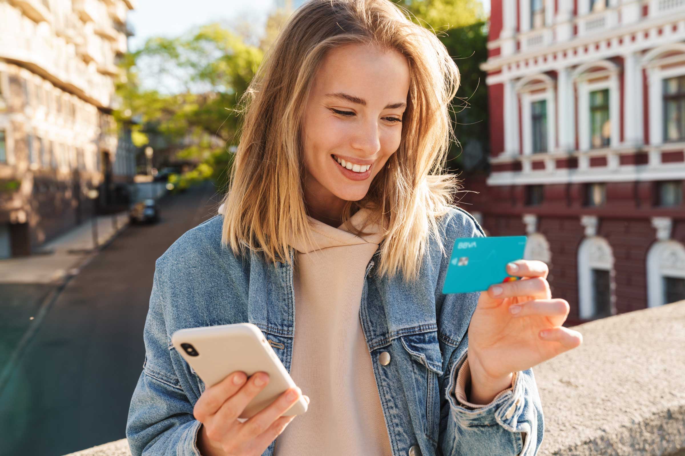 Eine Frau hält ihre neue BBVA Debitkarte in der linken Hand und ein Smartphone in der rechten Hand.