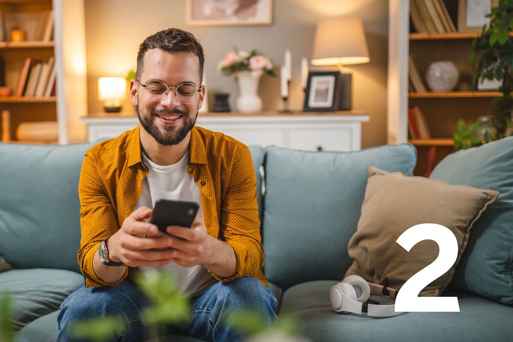 Ein Mann auf dem Sofa gibt Reisedaten und Teilnehmer für die Reiseversicherung in sein Smartphone ein.