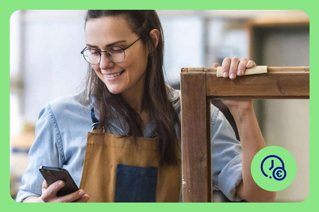 A person in a workshop is holding a wooden frame while looking at a smartphone – a symbol for flexible financing options such as instant loans.