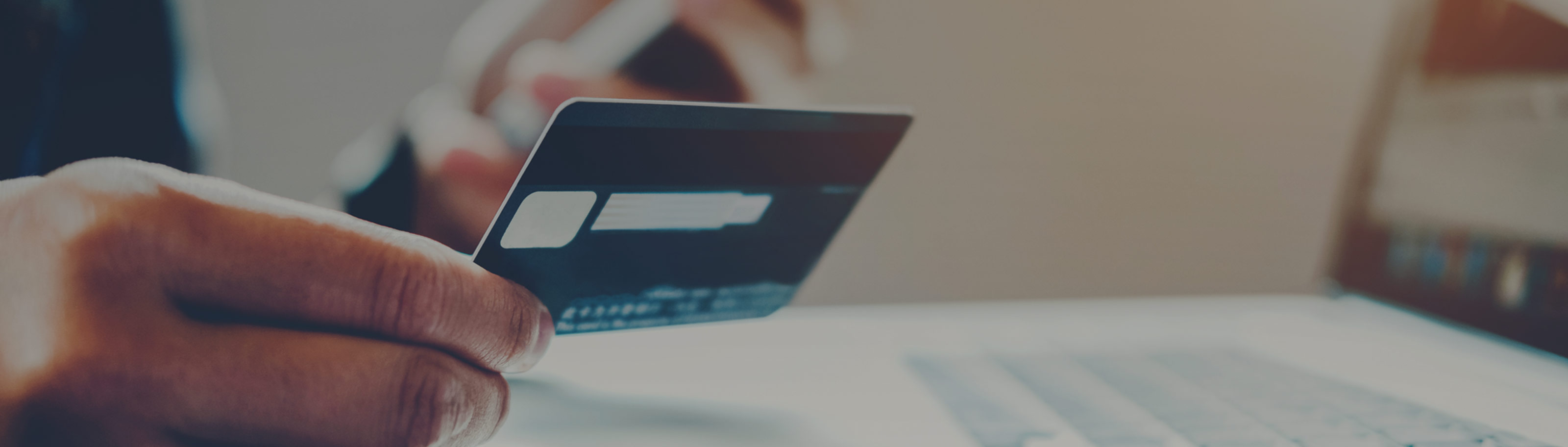 Hand hält eine Debitkarte vor einem Laptop – Symbolbild für Artikel zum Thema PayPal Debitkarte.