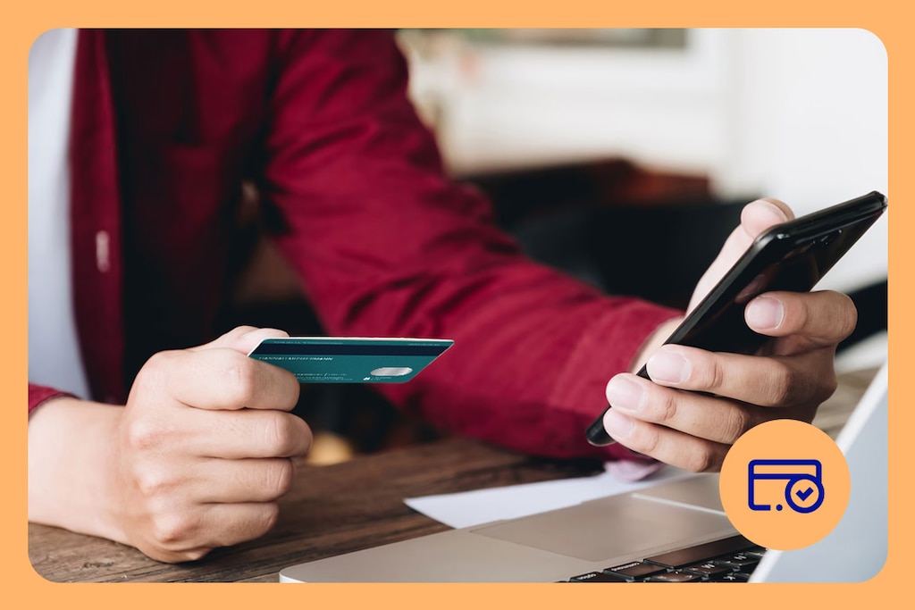 Person sitting in front of an open laptop, holding a debit card and a smartphone in their hands.